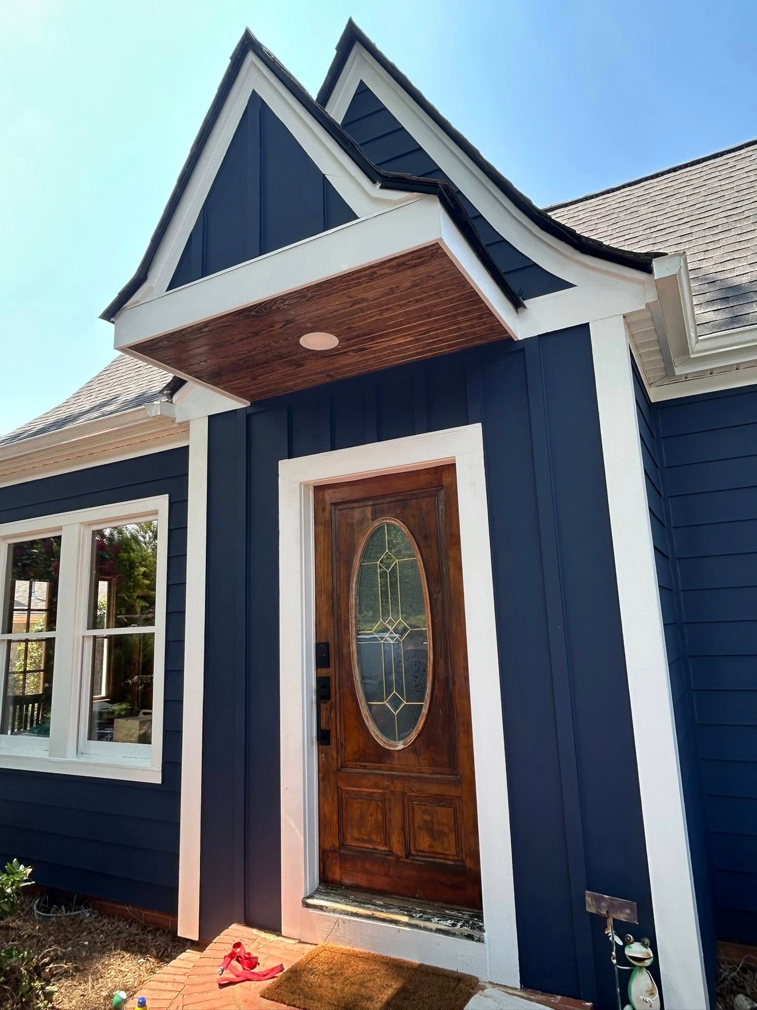 A dark blue house exterior features a front door with a decorative oval glass pane under a small, peaked roof entryway.