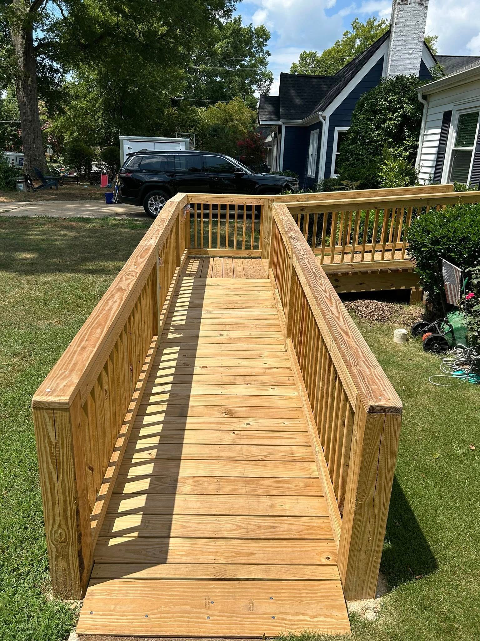 A wooden wheelchair ramp with side railings leading toward the entrance of a house on a sunny day.