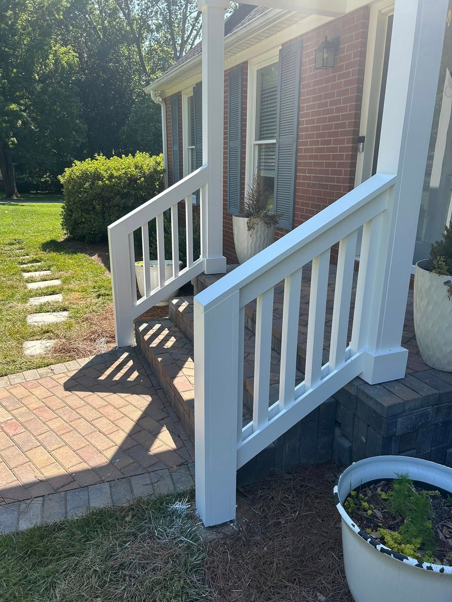 White wooden railings lining the concrete steps of a brick house with blue shutters.