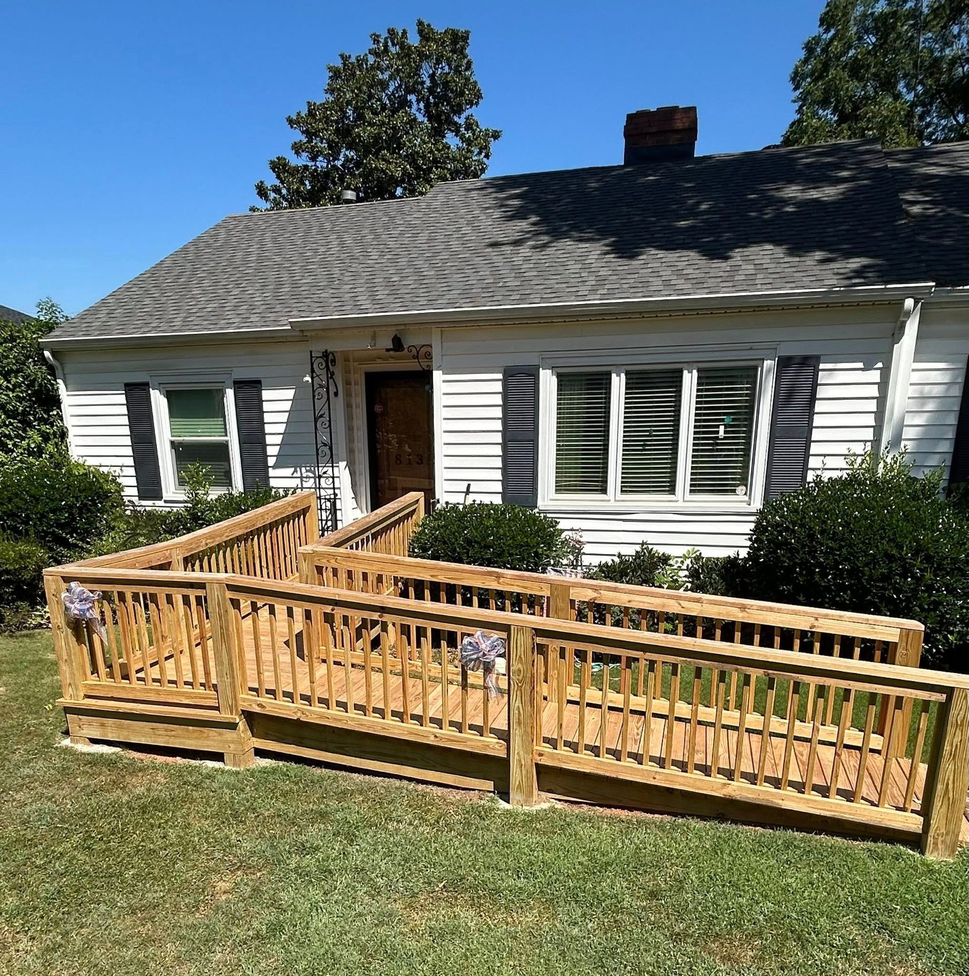 A wooden wheelchair ramp with railings installed in front of a white house with a brown door.