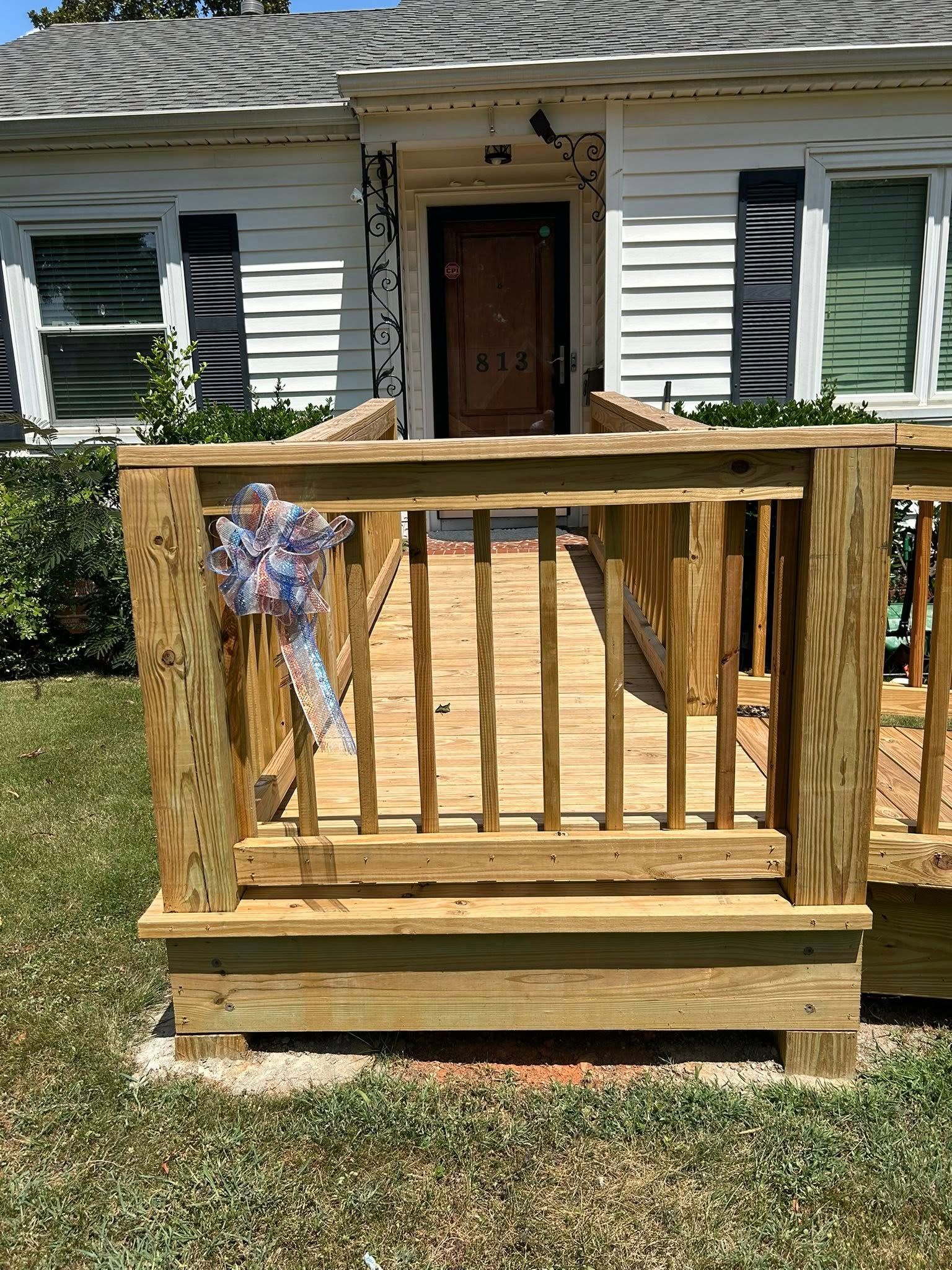 A wooden wheelchair ramp with railings leads to the front door of a white house.