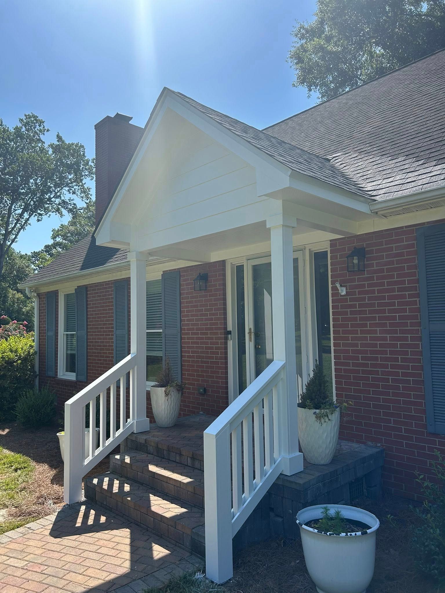 A brick house entrance featuring a white wooden gabled porch, white railings, and steps leading to the front door.
