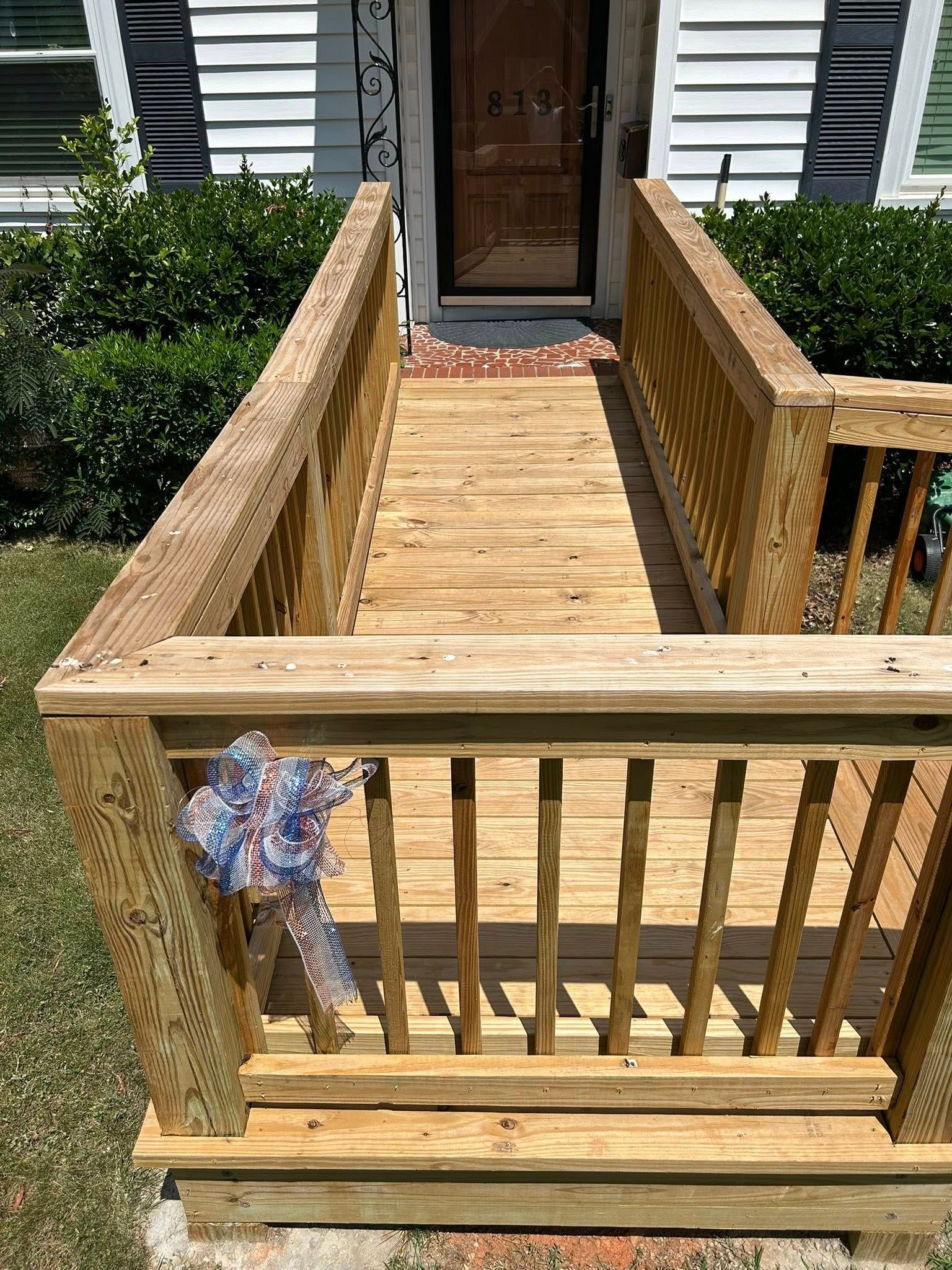 A wooden wheelchair ramp with railings leading up to a front door, decorated with a patriotic bow on the corner post.