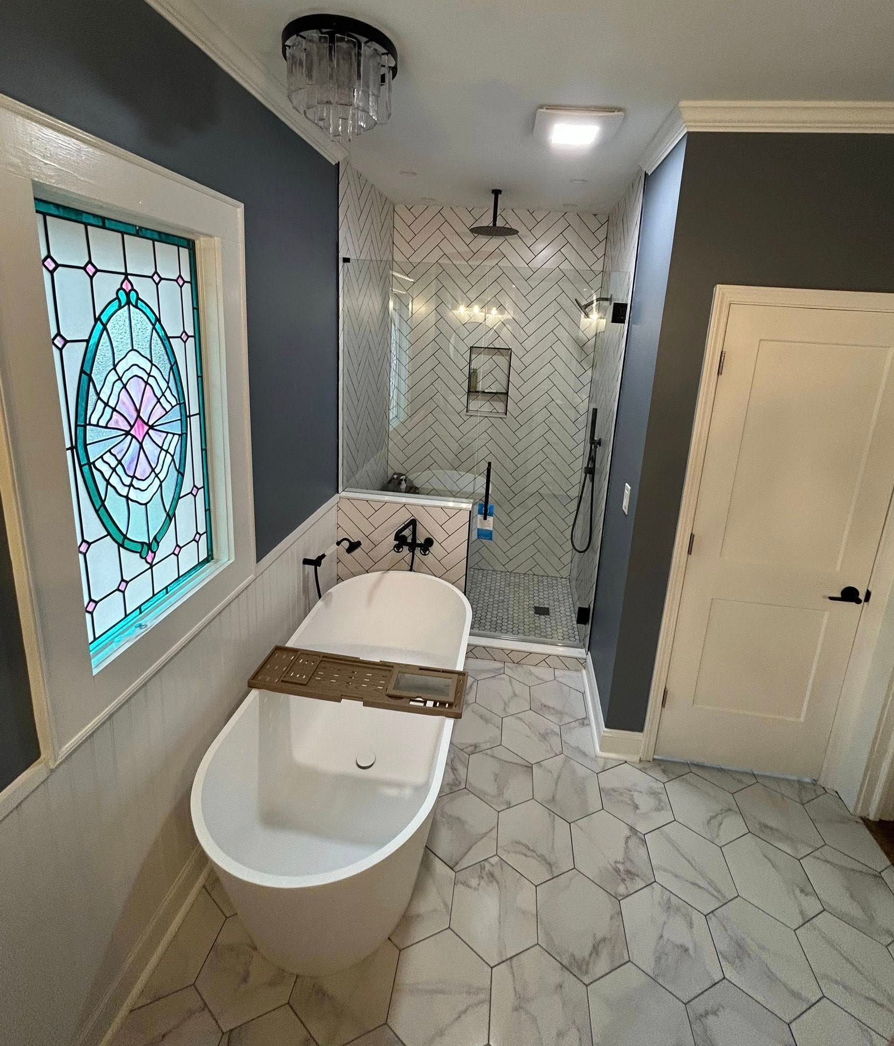 A modern bathroom featuring a freestanding soaking tub, a tiled walk-in shower, and a large stained-glass window.