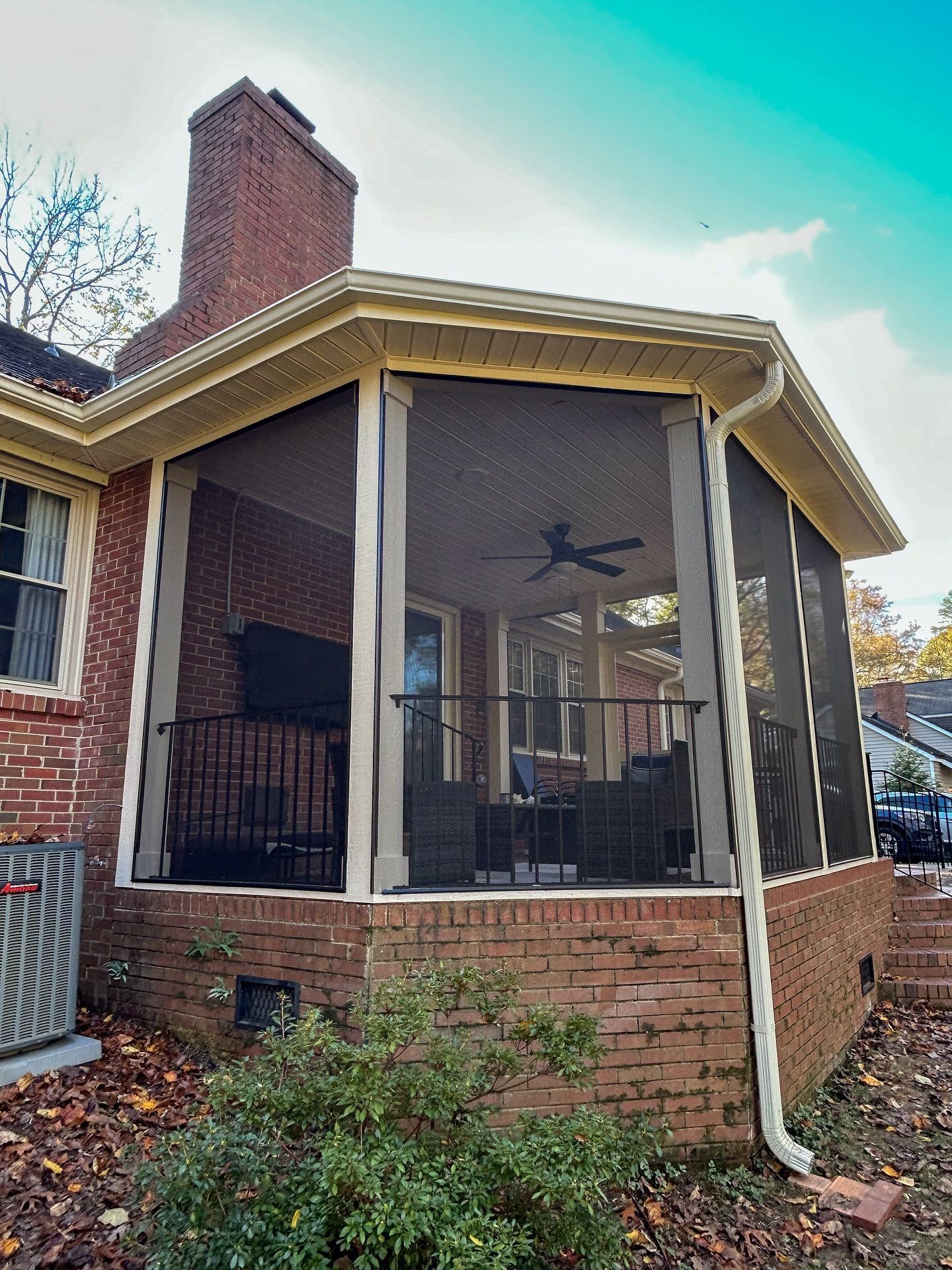 A screened-in brick porch addition with a ceiling fan, attached to a brick house with a chimney.