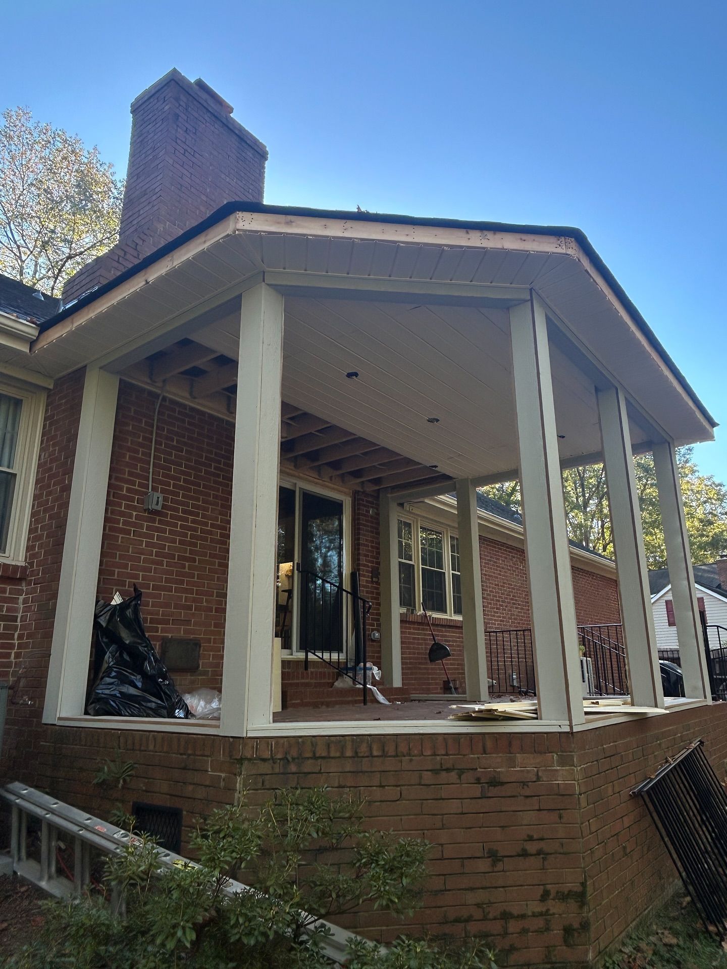 A brick house with a partially renovated front porch featuring white wooden pillars and an unfinished ceiling.
