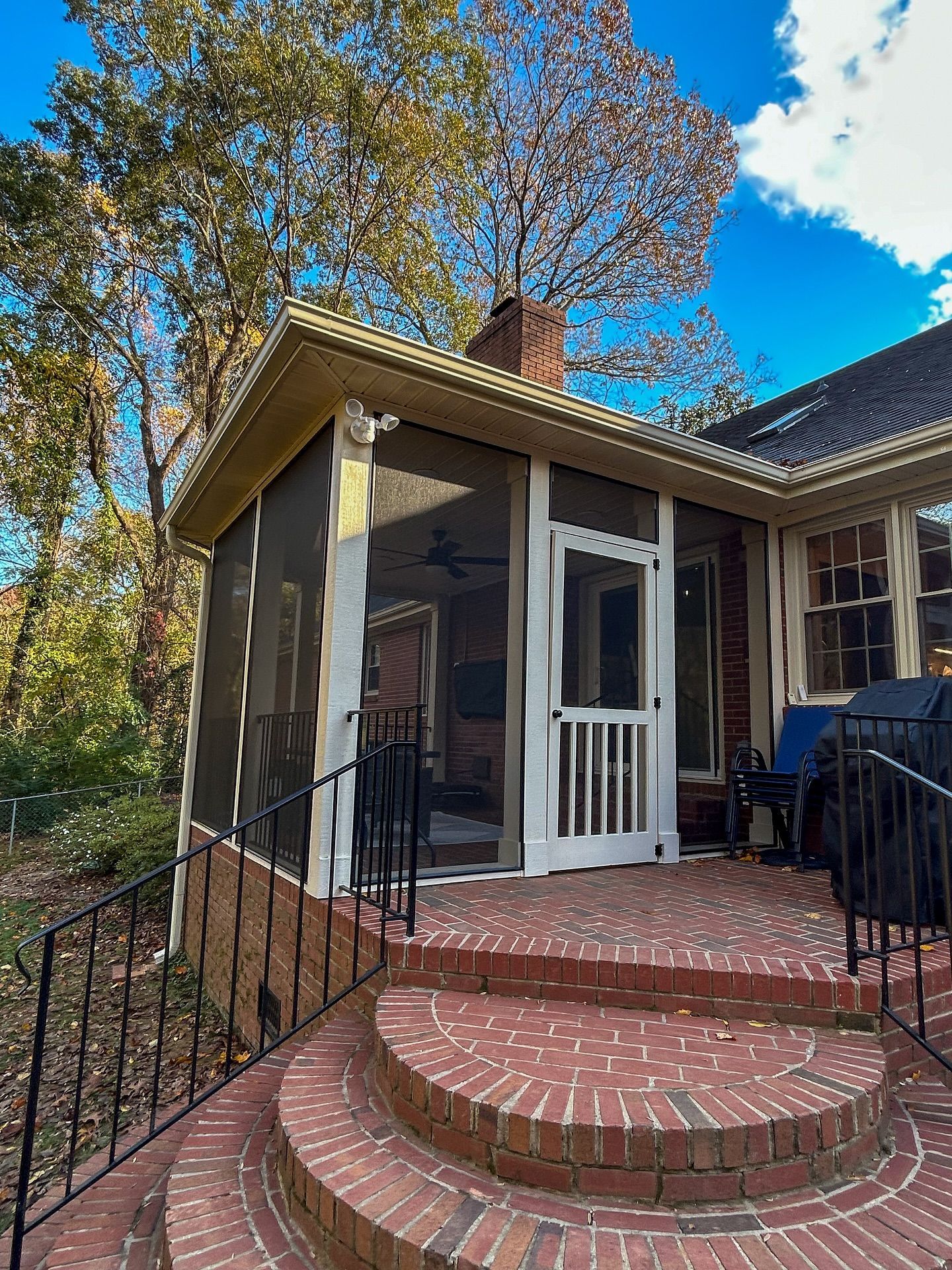 A brick patio with curved steps leads to a screened-in porch on a house exterior under a clear blue sky.