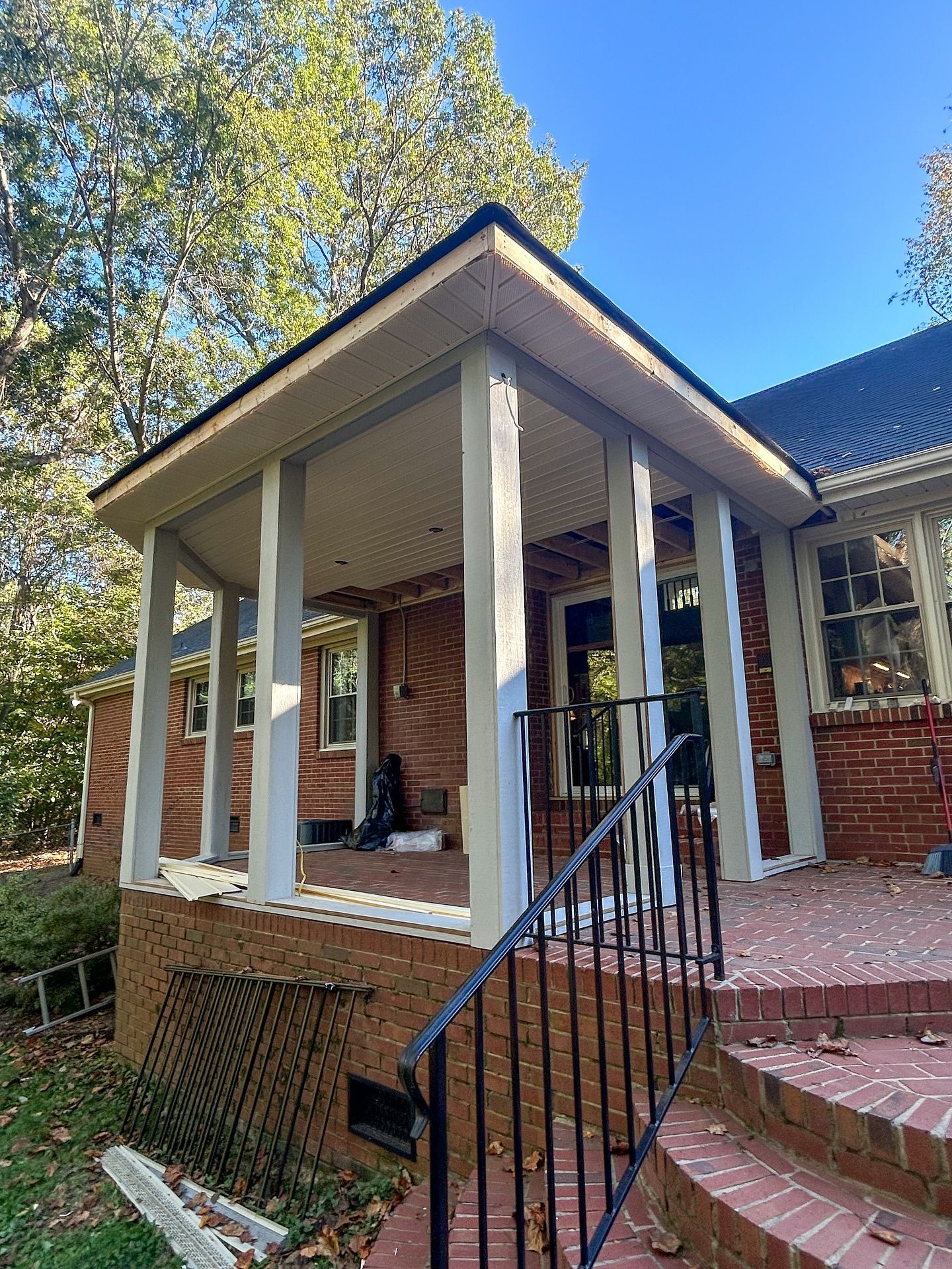 A red brick house with a covered porch featuring white support columns and steps leading to a side entrance.