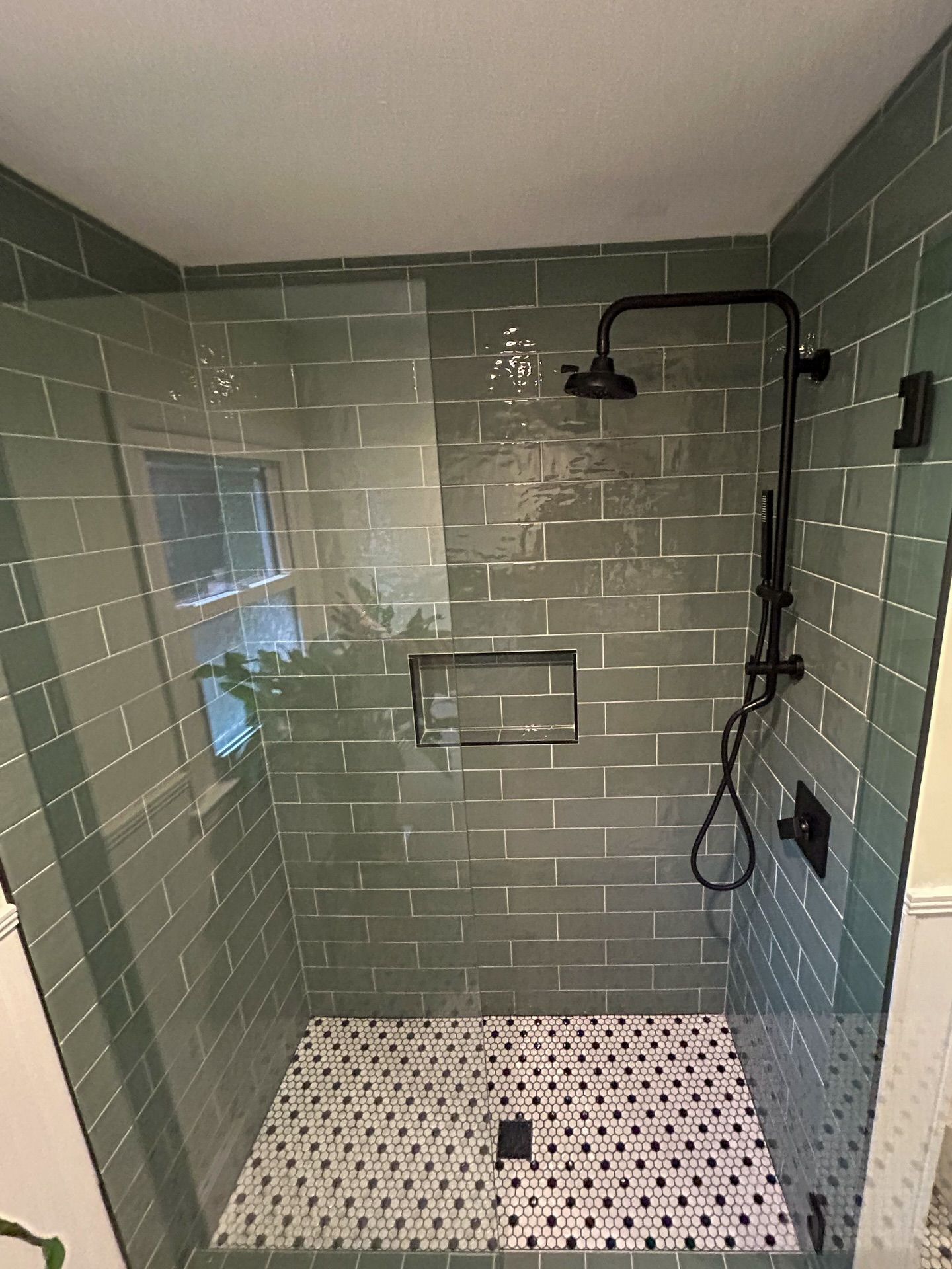 A modern walk-in shower with green subway wall tiles, black fixtures, and a white and black mosaic tile floor.