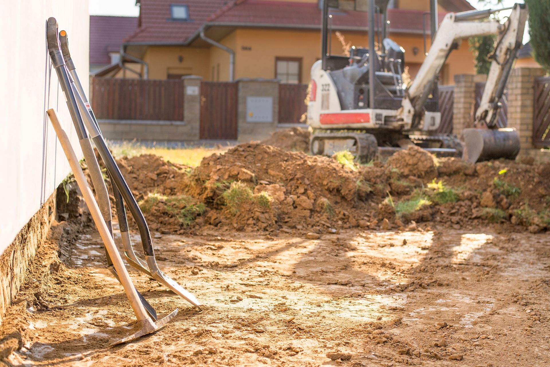 An excavator is digging a hole in the dirt in front of a house.
