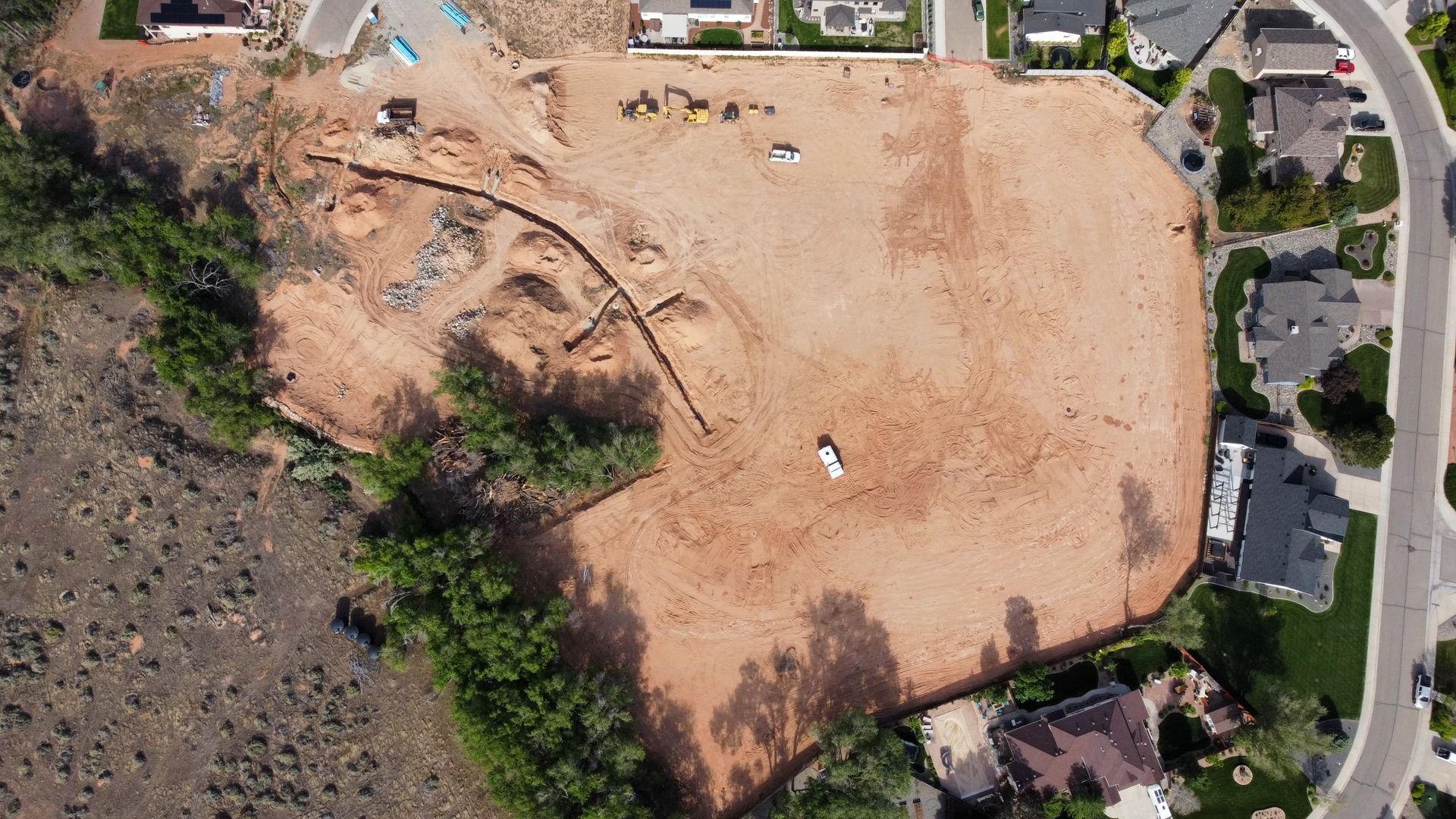 An aerial view of a large dirt field with houses in the background.
