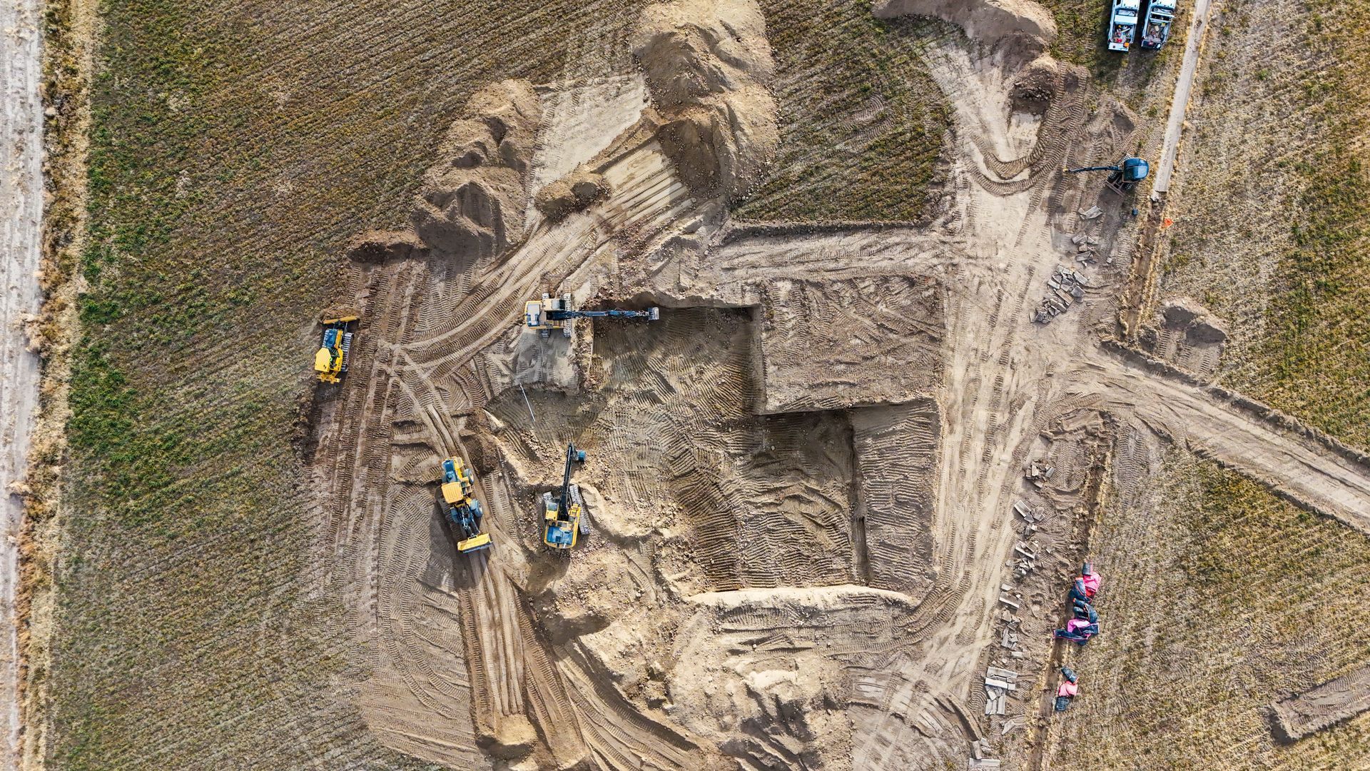 Aerial view of a construction site showing multiple excavators digging in a field.