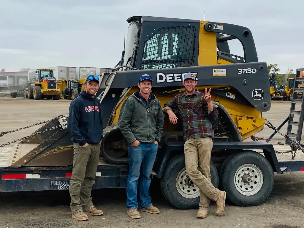 Three men are standing next to a trailer with a bulldozer on it.