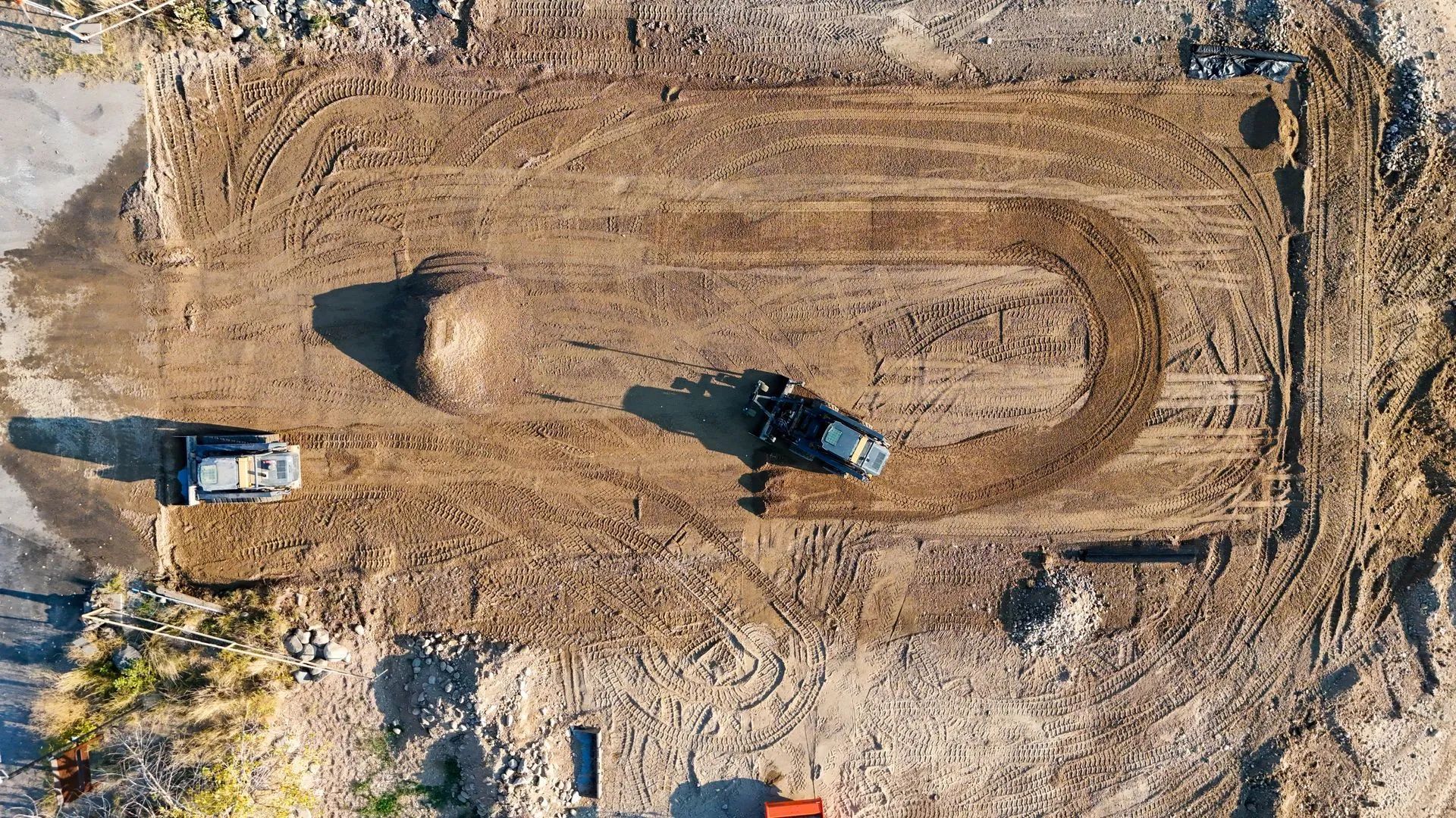 Aerial view of two construction vehicles shaping a dirt track.