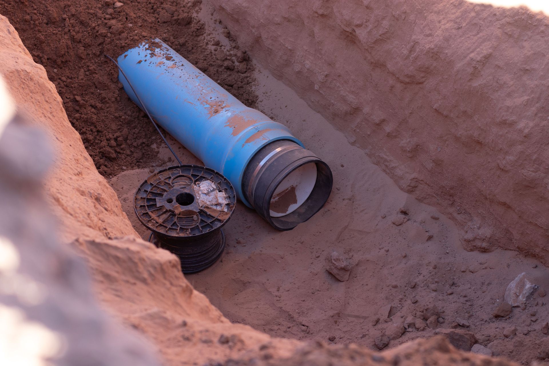 Blue pipe section and wire spool in an excavated trench.