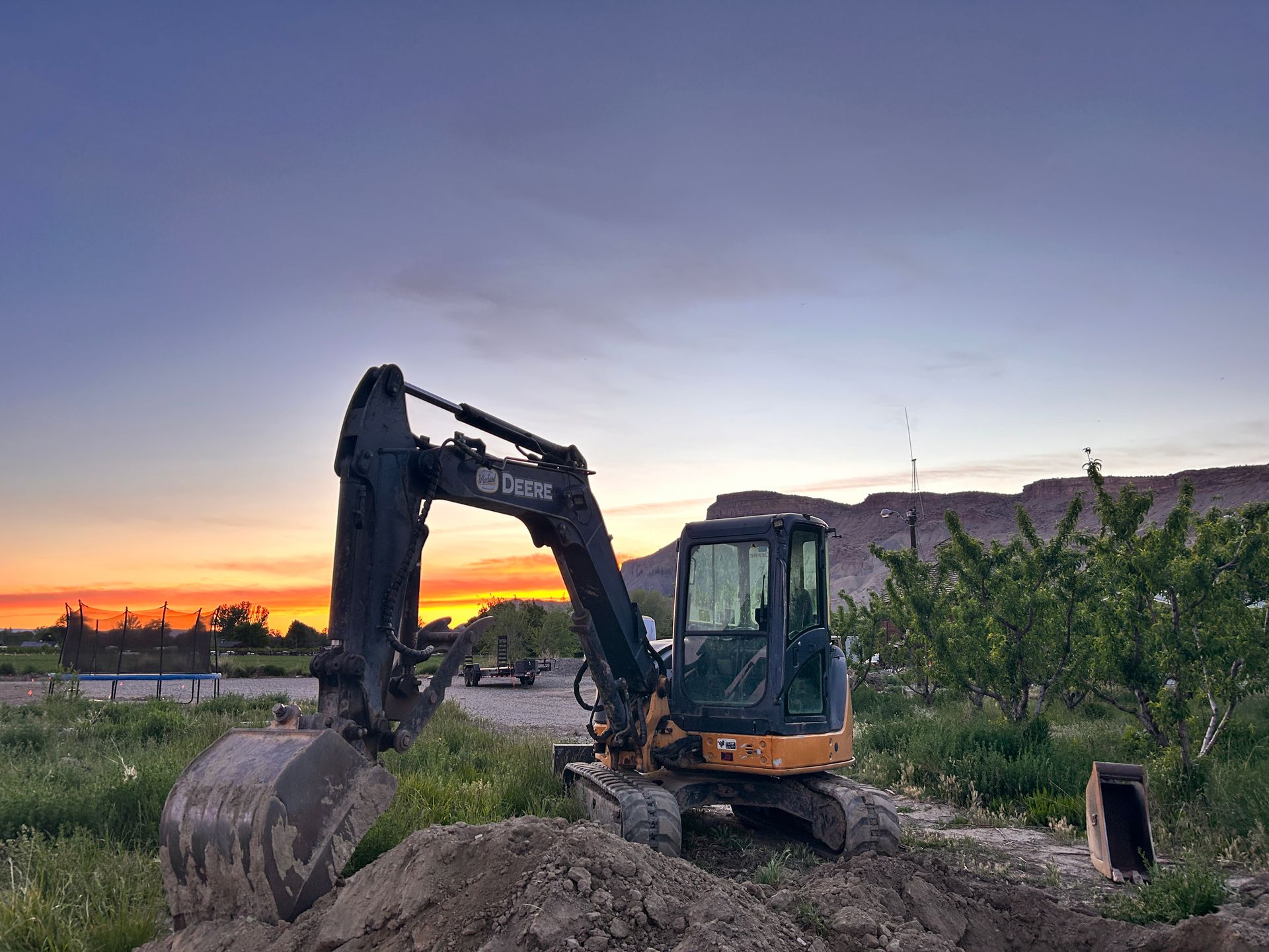 Excavator on a construction site at sunset, with a mountain in the background.