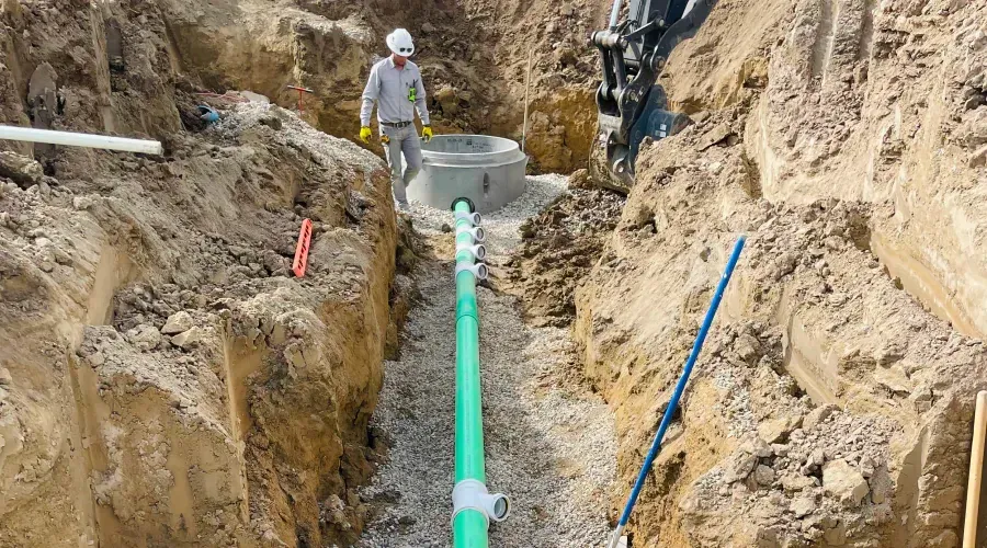 A man is standing in a trench next to a green pipe.