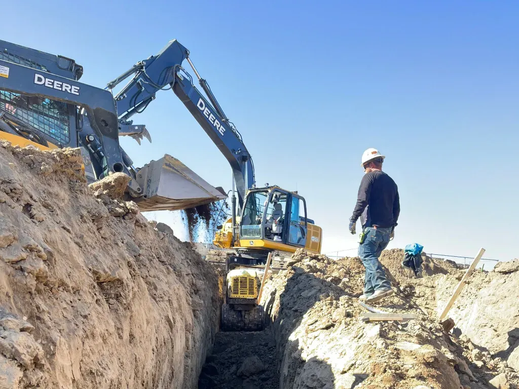 A man is standing in a trench next to a large excavator.