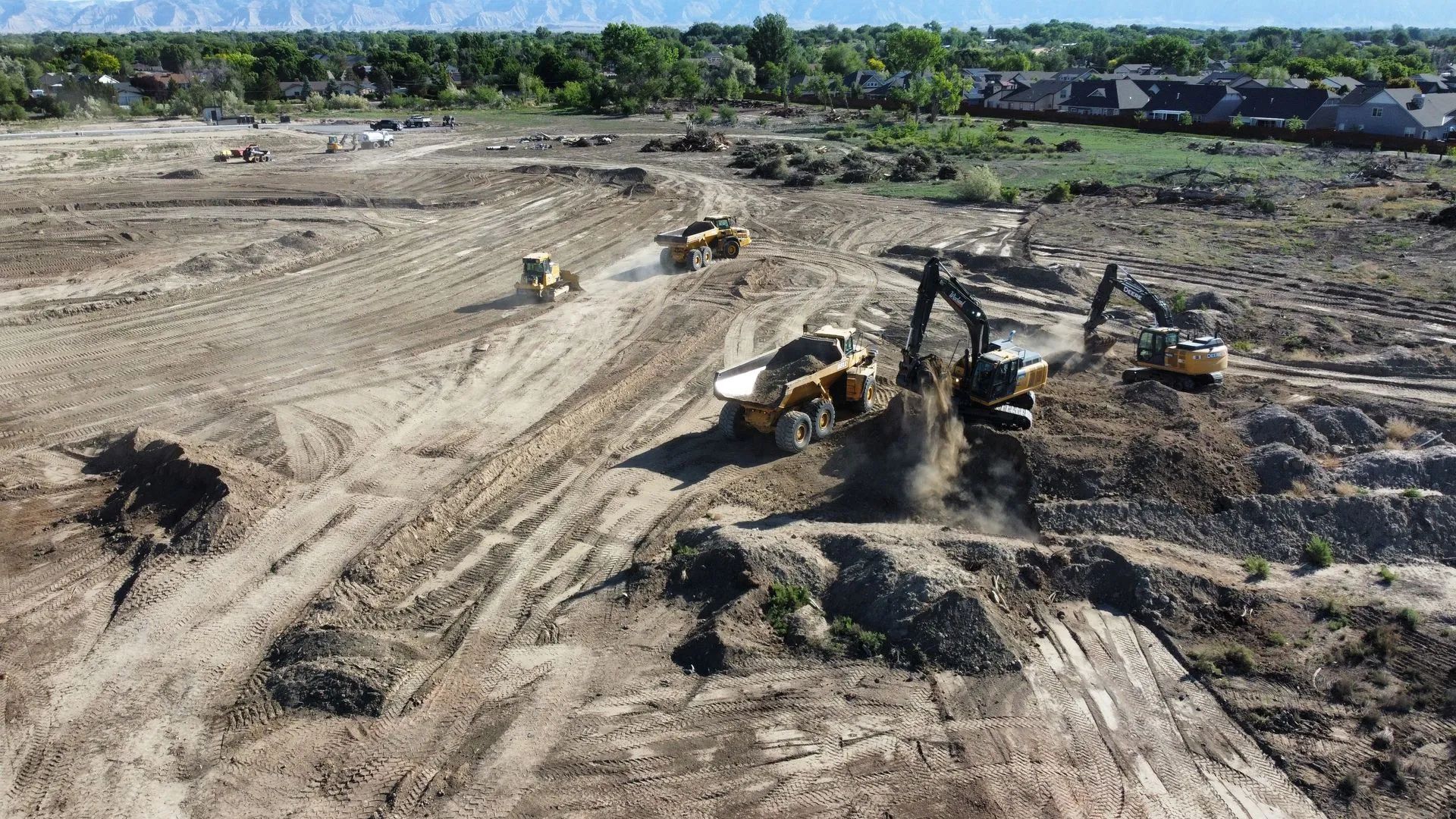 Construction site with several heavy machines: bulldozers, excavators, and dump trucks. Earthmoving in progress.