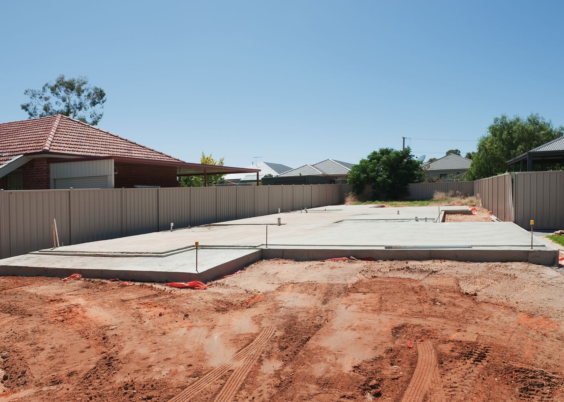 A concrete foundation is being built on a dirt lot in front of a house.