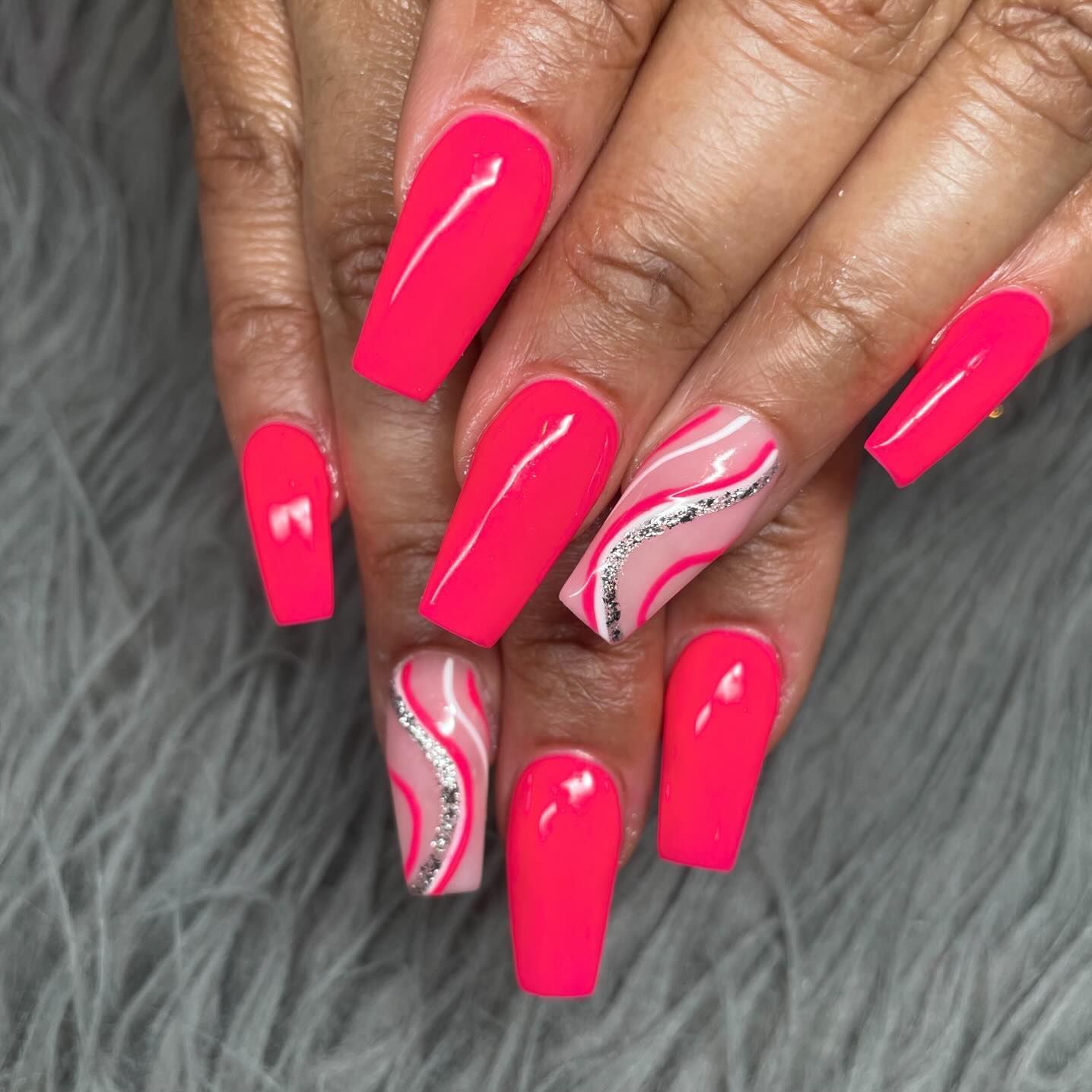 A woman 's nails are long and bright pink with a silver design.