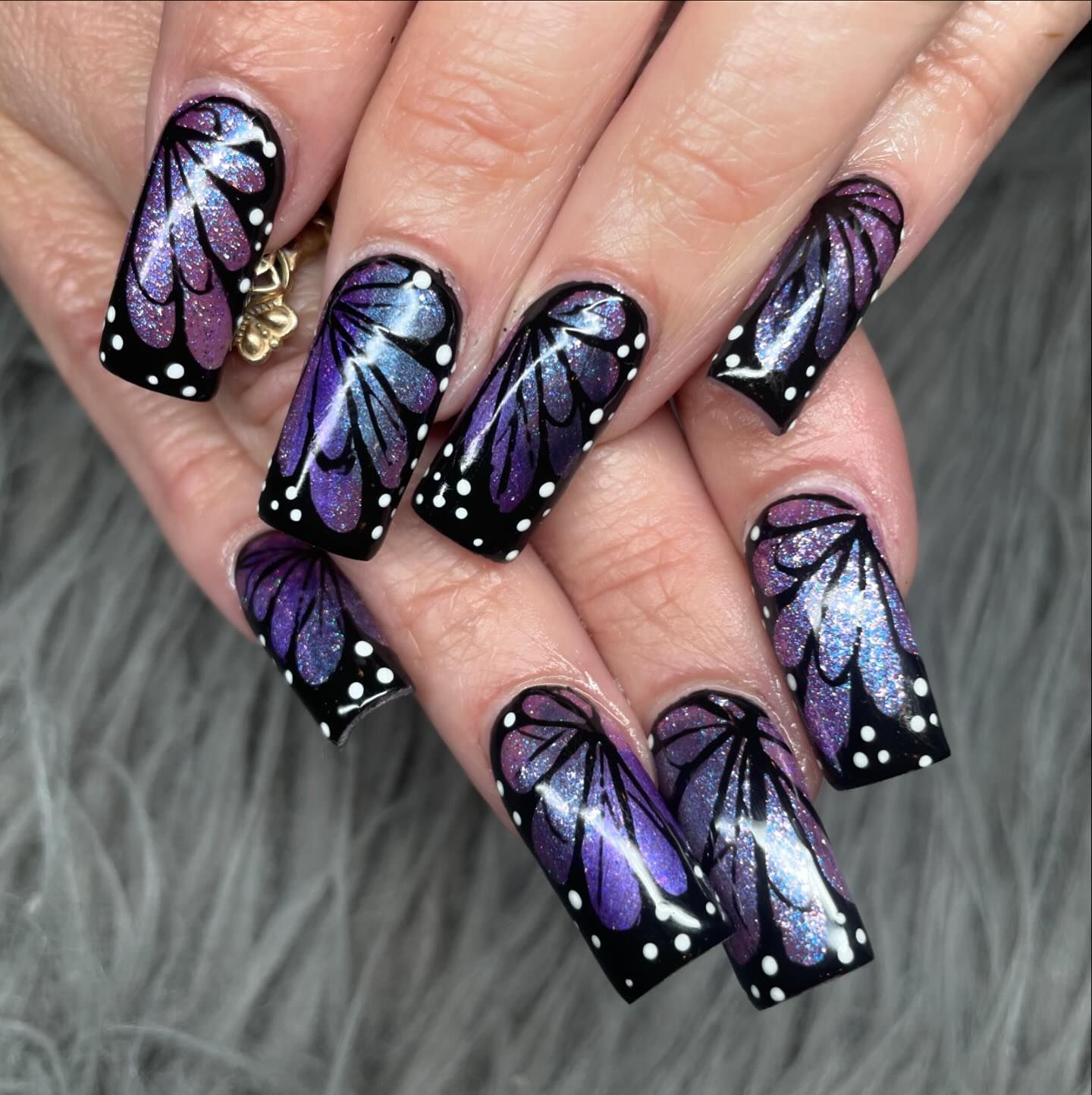 A woman 's nails are painted in purple and black with a butterfly design