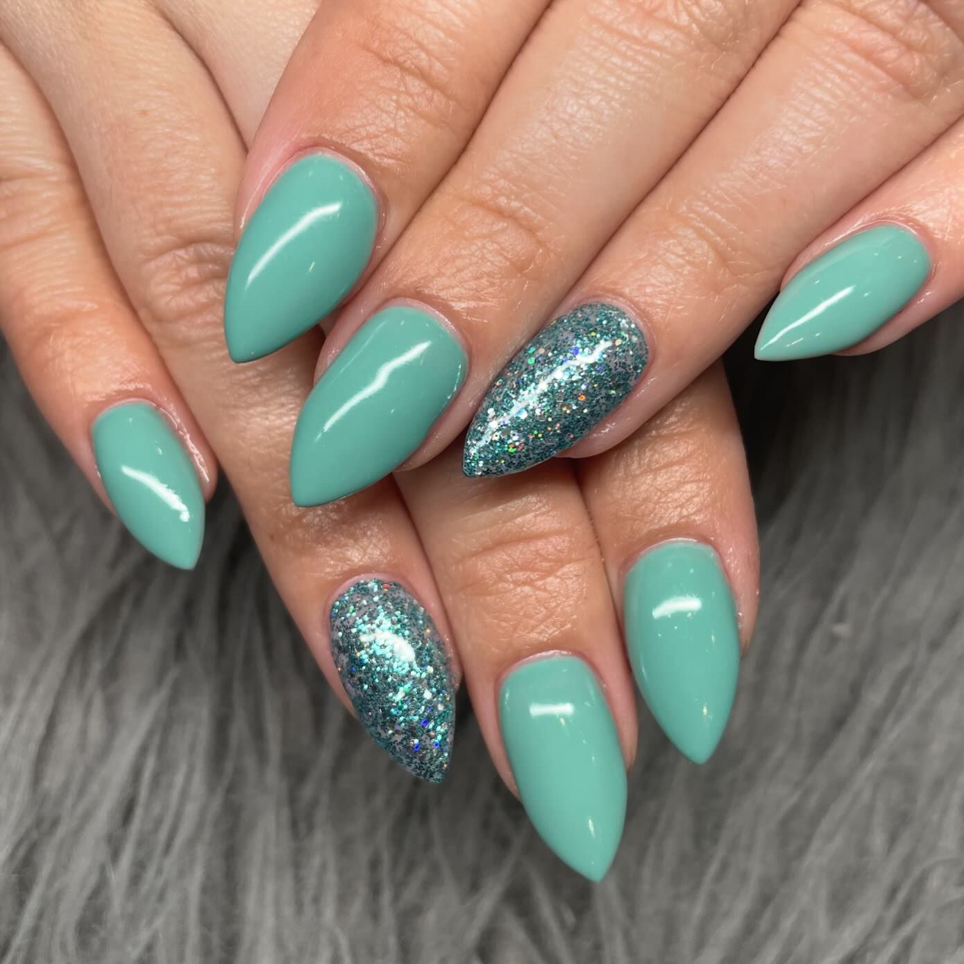 A close up of a woman 's nails with green nail polish and glitter.