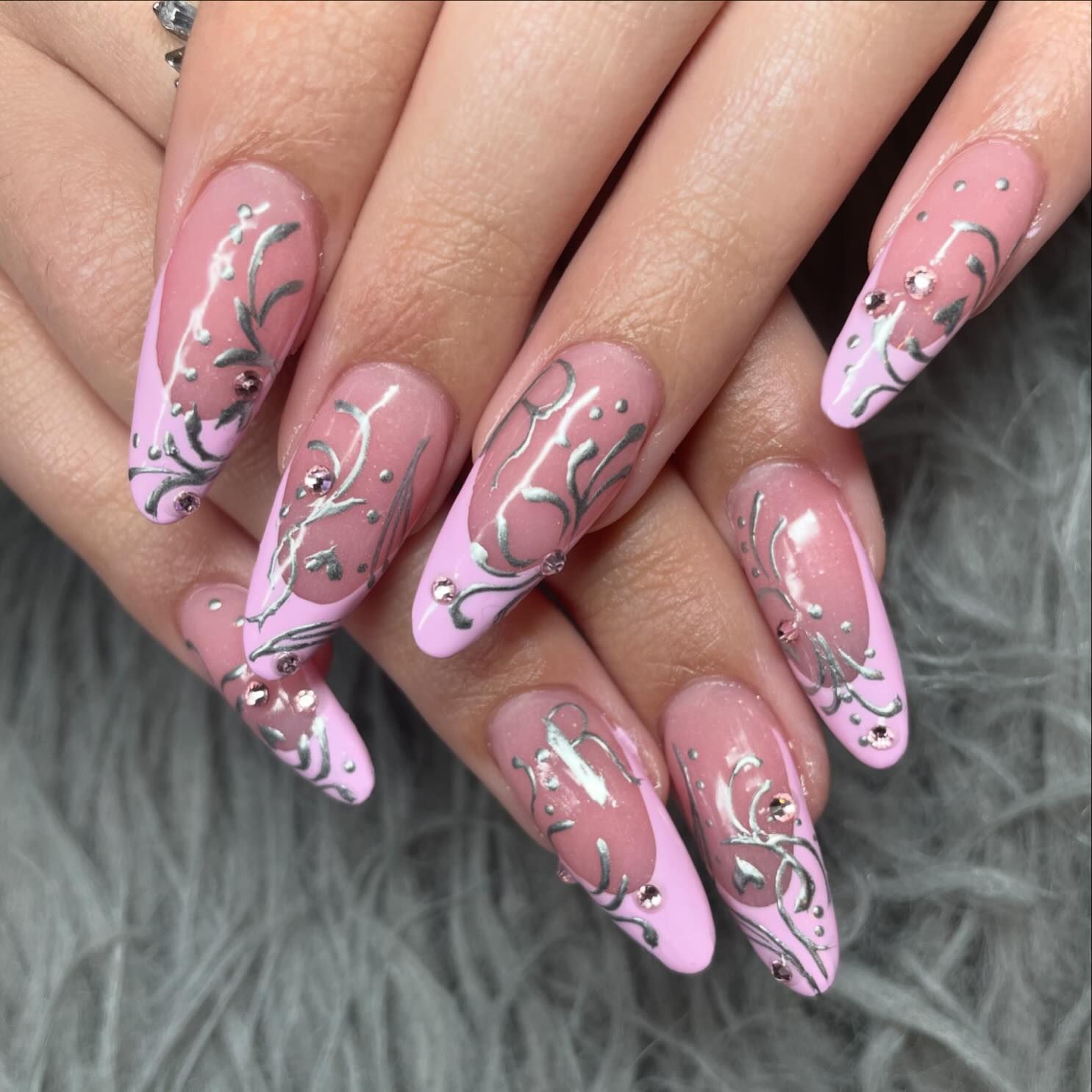 A close up of a woman 's nails with pink and silver designs