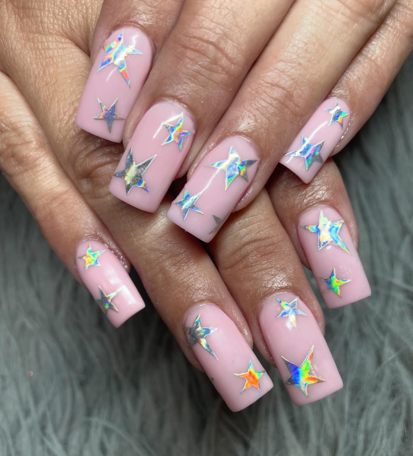 A close up of a woman 's pink nails with holographic stars on them.