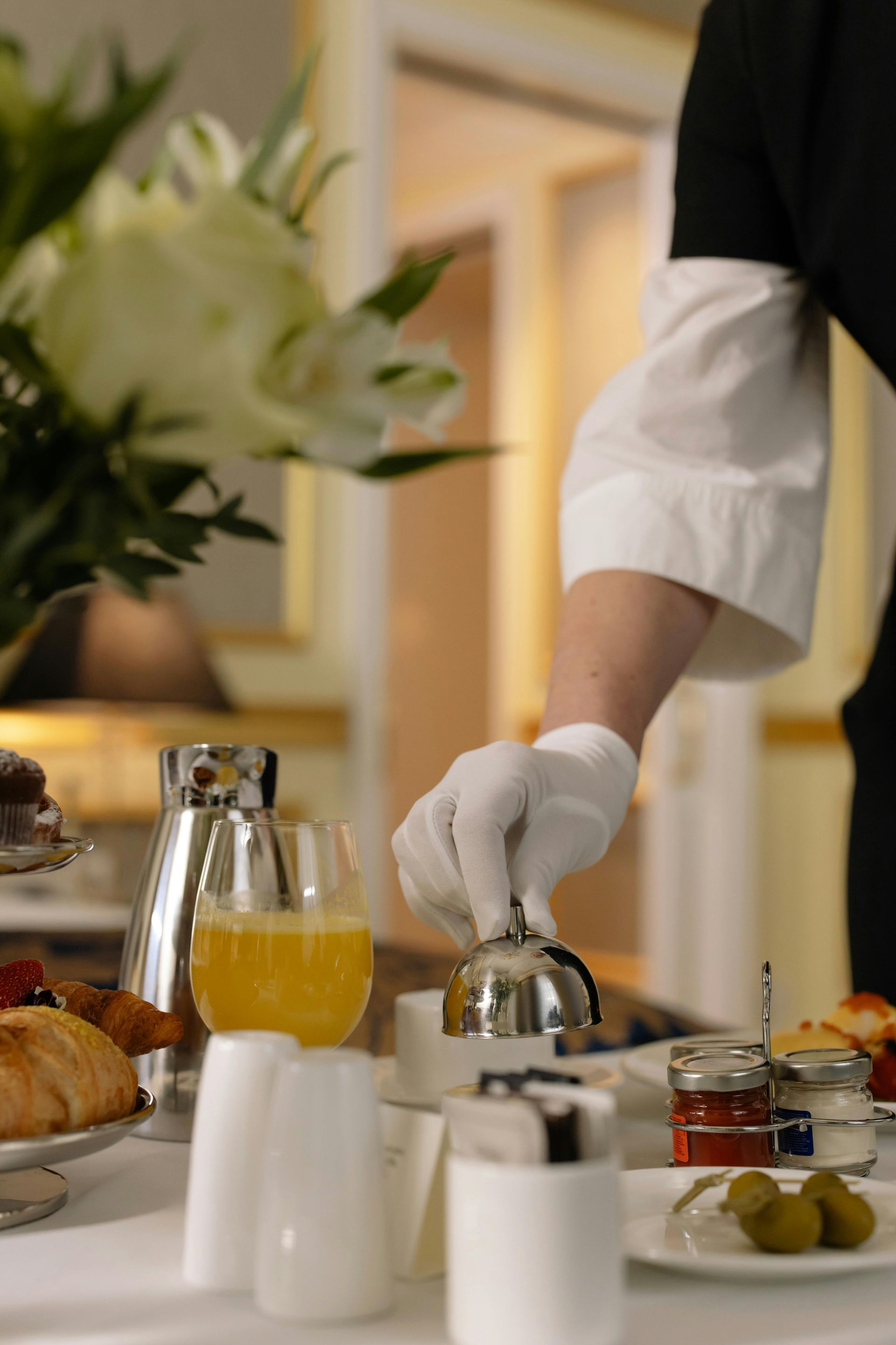 Cameriere che versa il caffè a un tavolo per la colazione con pasticcini, succo di frutta e fiori.
