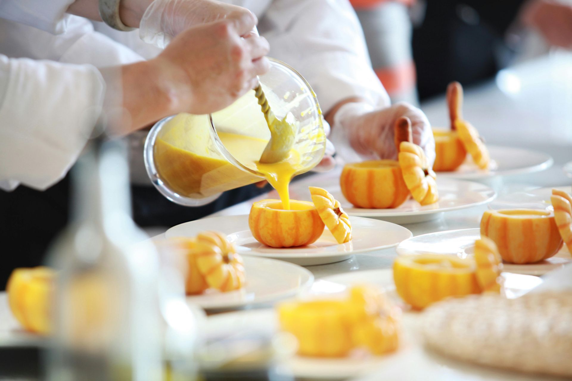 Mani che versano salsa gialla su piccoli dessert arancioni a forma di zucca su piatti bianchi.