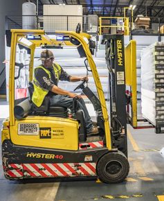 A man is driving a yellow forklift in a warehouse.