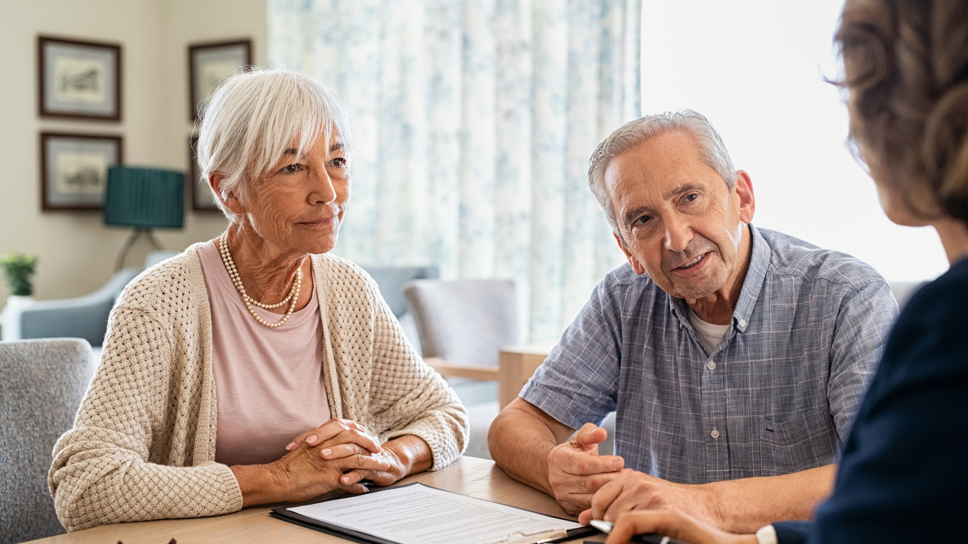 Older couple at table with a person, reviewing paperwork, discussing something.