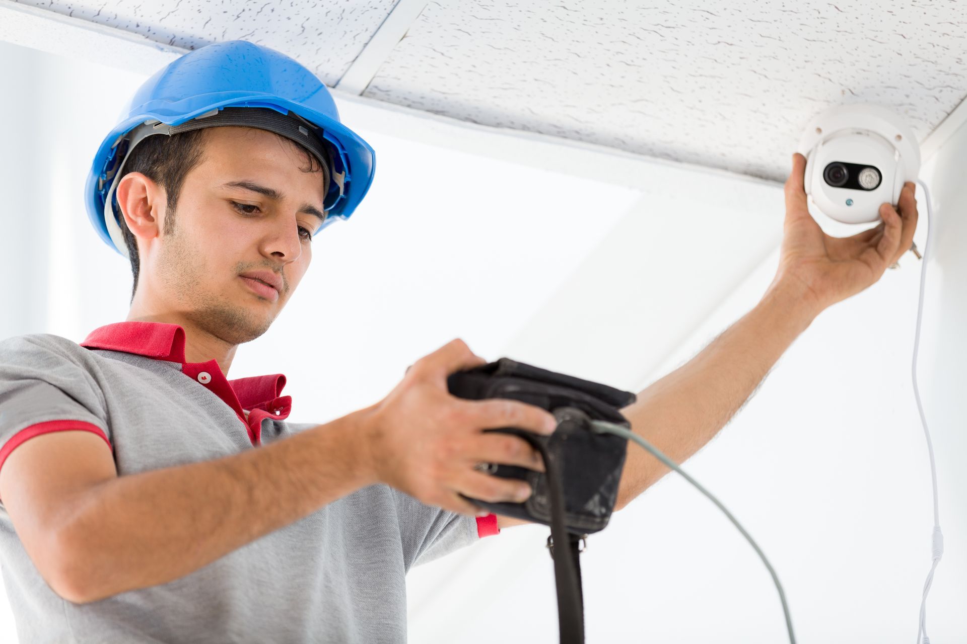 Electrician mounting a security camera on the ceiling for enhanced safety and surveillance.