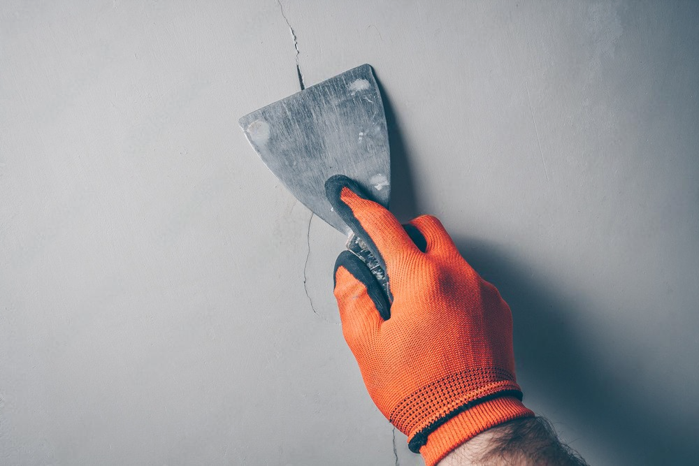 a person is holding a spatula and plastering a wall .