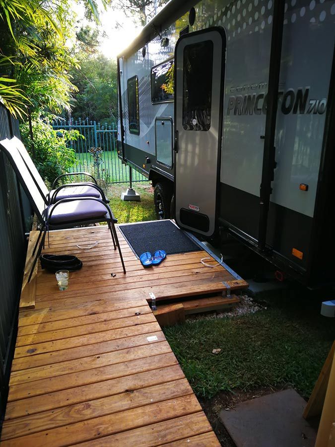 A Caravan Is Parked Next To A Wooden Deck With Chairs On It — Perkins Caravans in Ballina, NSW