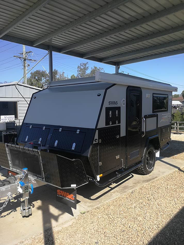 A Black And White Camper Trailer Is Parked Under A Covered Area — Perkins Caravans in Grafton, NSW