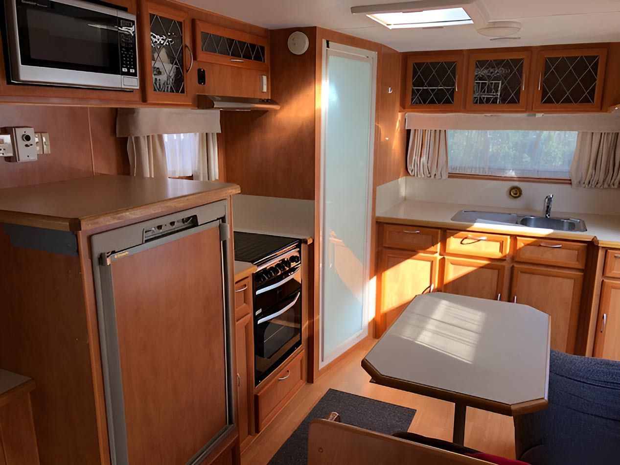 A Kitchen In A Camper With Wooden Cabinets And A Table — Perkins Caravans in Grafton, NSW