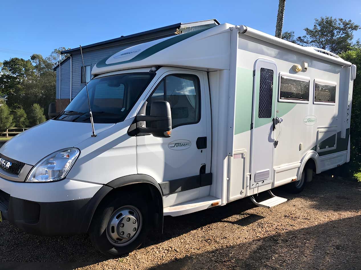 A White Motorhome Is Parked In A Gravel Lot In Front Of A Building — Perkins Caravans in Yamba, NSW