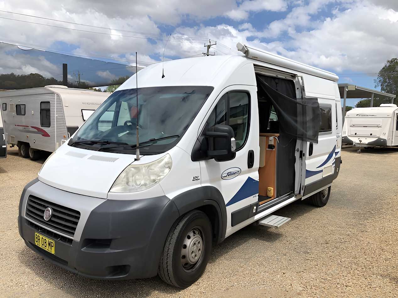 A White Motorhome With The Door Open Is Parked In A Gravel Lot — Perkins Caravans in Byron Bay, NSW