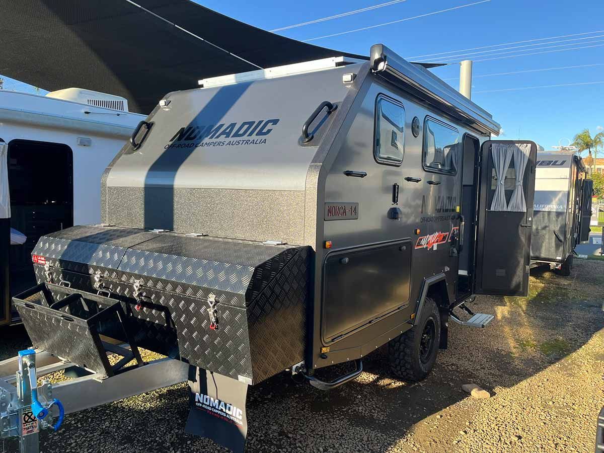 A Black And Gray Camper Trailer Is Parked In A Gravel Lot — Perkins Caravans in Ballina, NSW