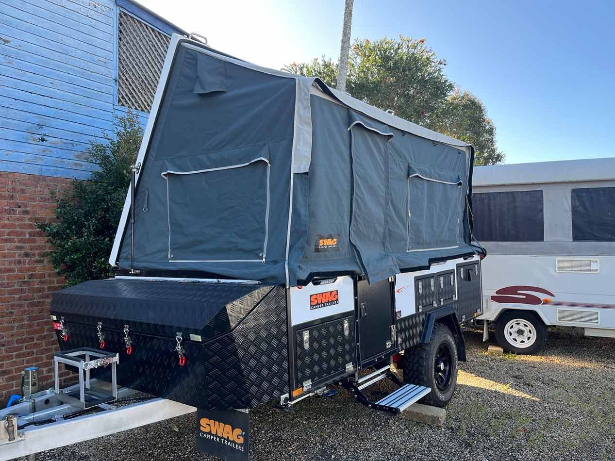 A Trailer With A Tent On Top Of It Is Parked In A Gravel Lot — Perkins Caravans in Ballina, NSW