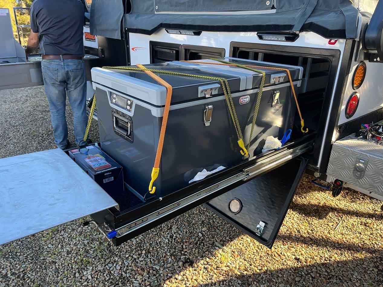 A Man Is Loading A Cooler Into The Back Of A Trailer — Perkins Caravans in Ballina, NSW
