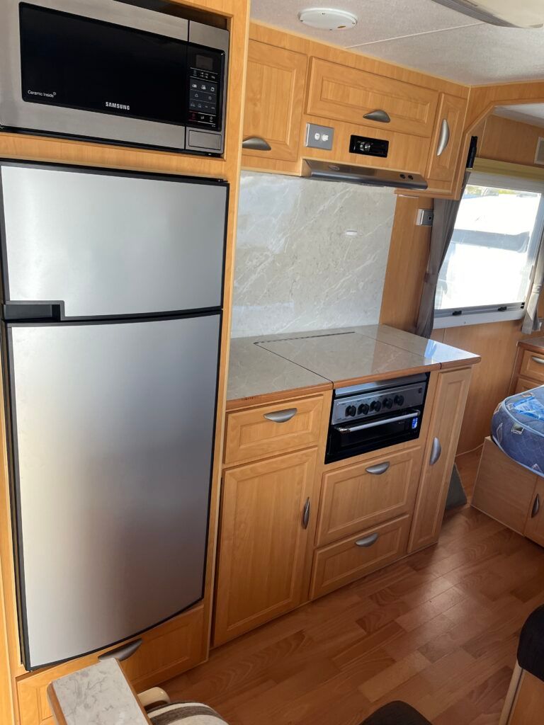 A Kitchen In A Camper With Stainless Steel Appliances And Wooden Cabinets — Perkins Caravans in Ballina, NSW