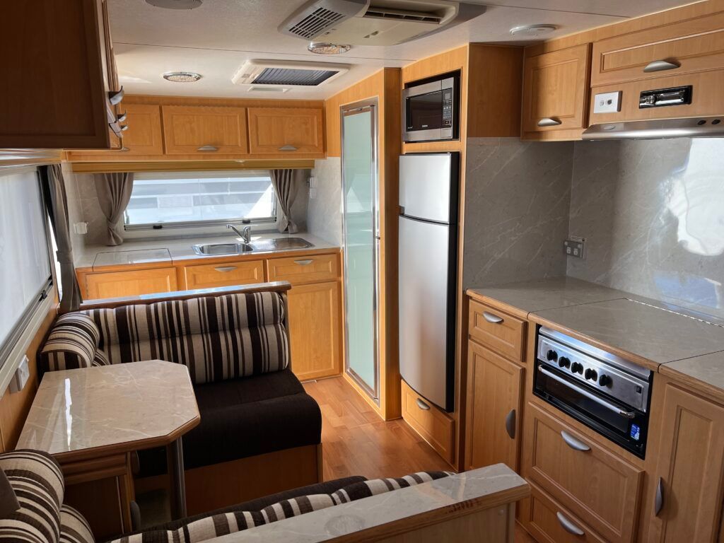 A Kitchen In A Camper With Wooden Cabinets And A Refrigerator — Perkins Caravans in Ballina, NSW