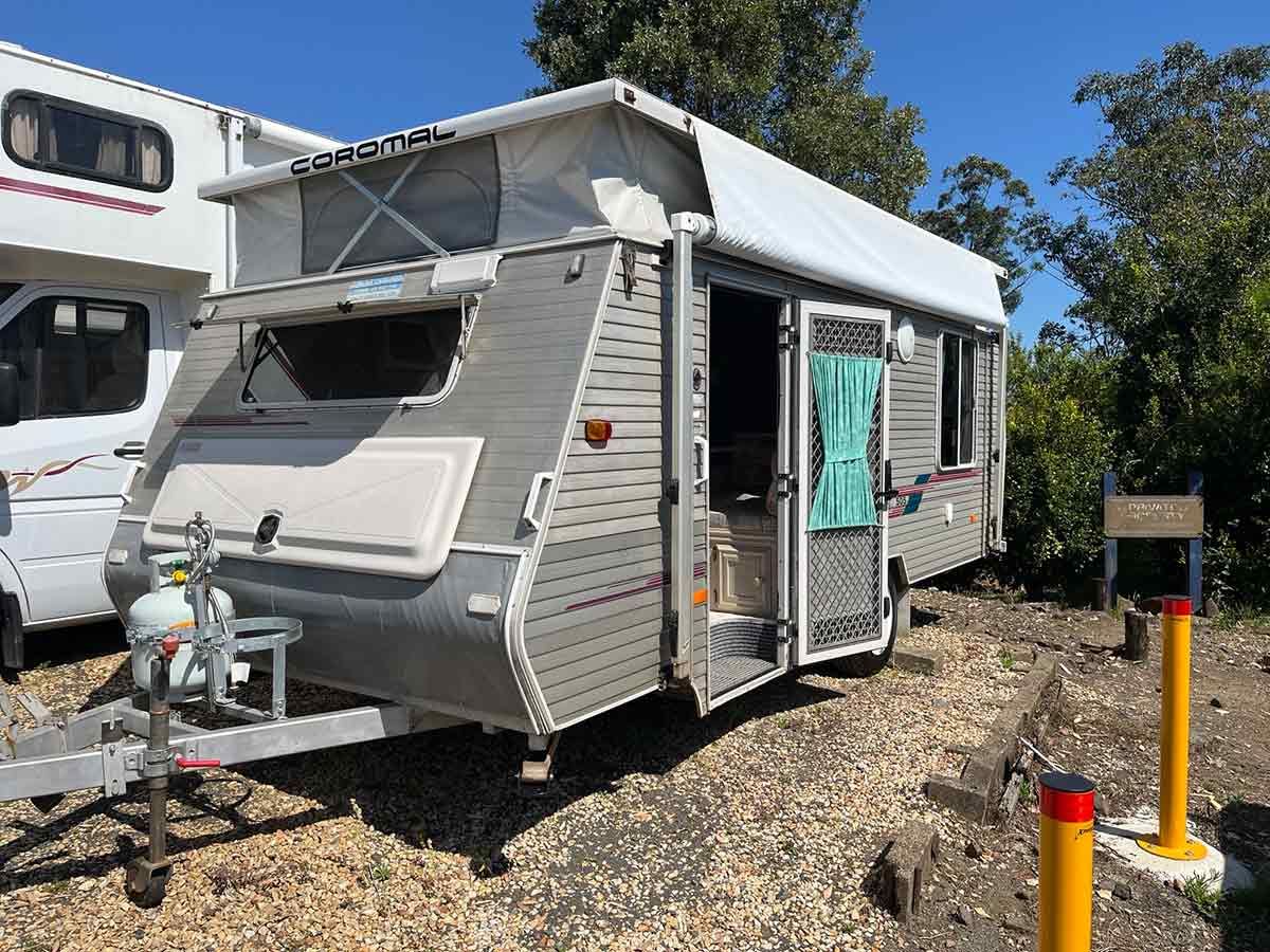 A Camper Trailer Is Parked In A Gravel Lot Next To A White Van — Perkins Caravans in Ballina, NSW