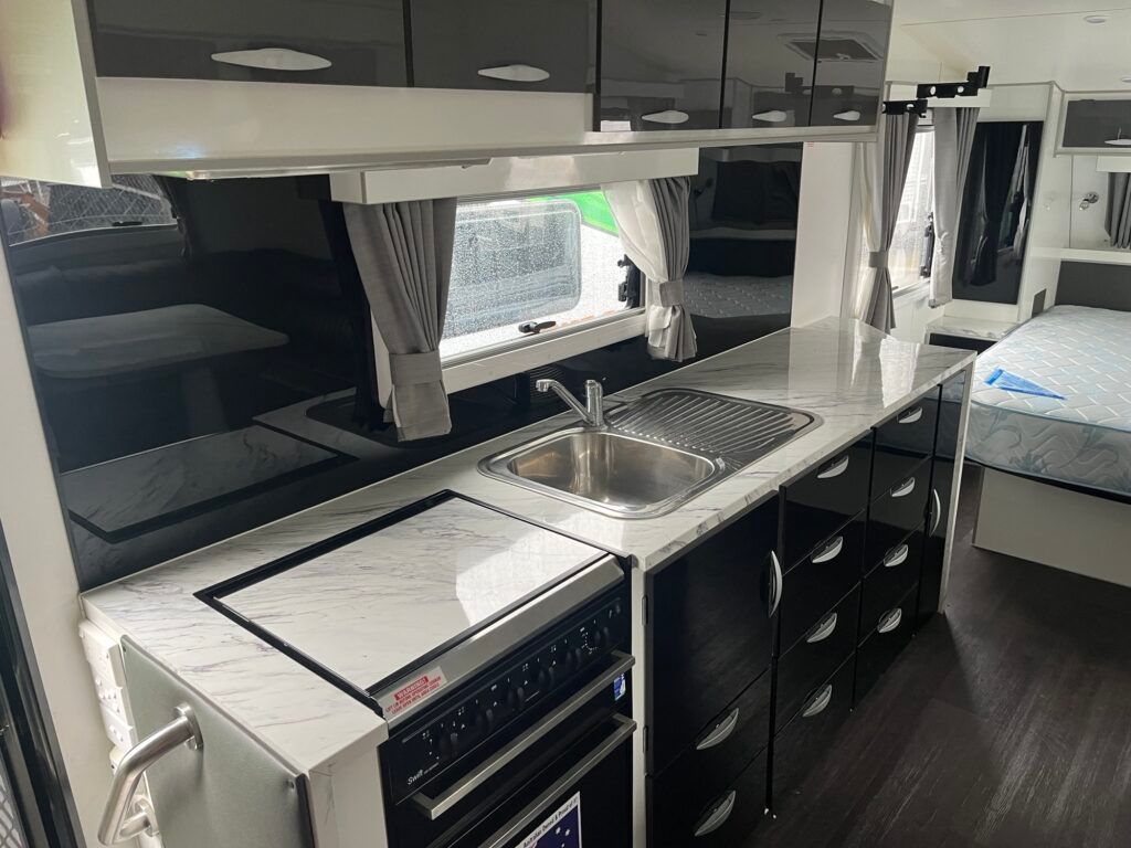 A Kitchen In A Camper With A Sink, Stove, And Cabinets — Perkins Caravans in Ballina, NSW