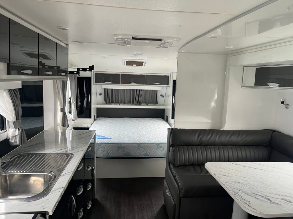 The Inside Of A Camper With A Bed, Couch, Table And Sink — Perkins Caravans in Ballina, NSW