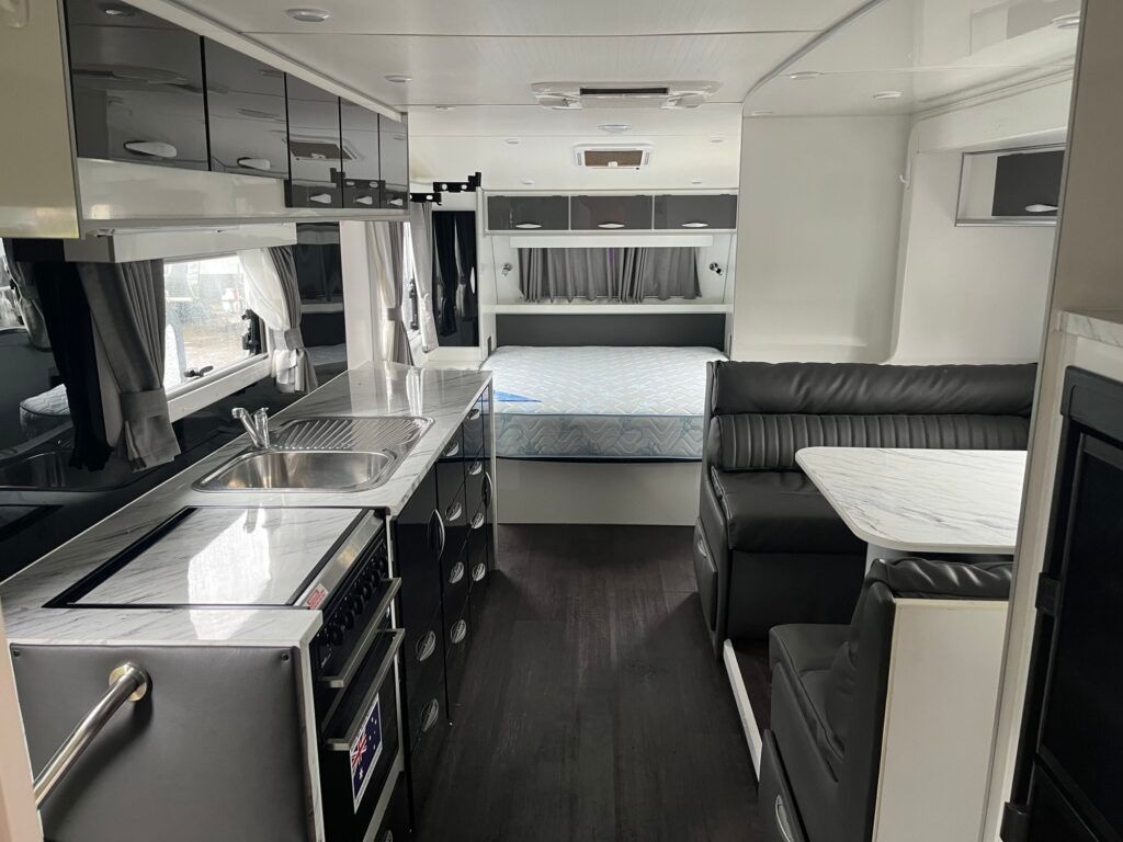 The Inside Of A Camper With A Kitchen, Couch, Table And Bed — Perkins Caravans in Ballina, NSW