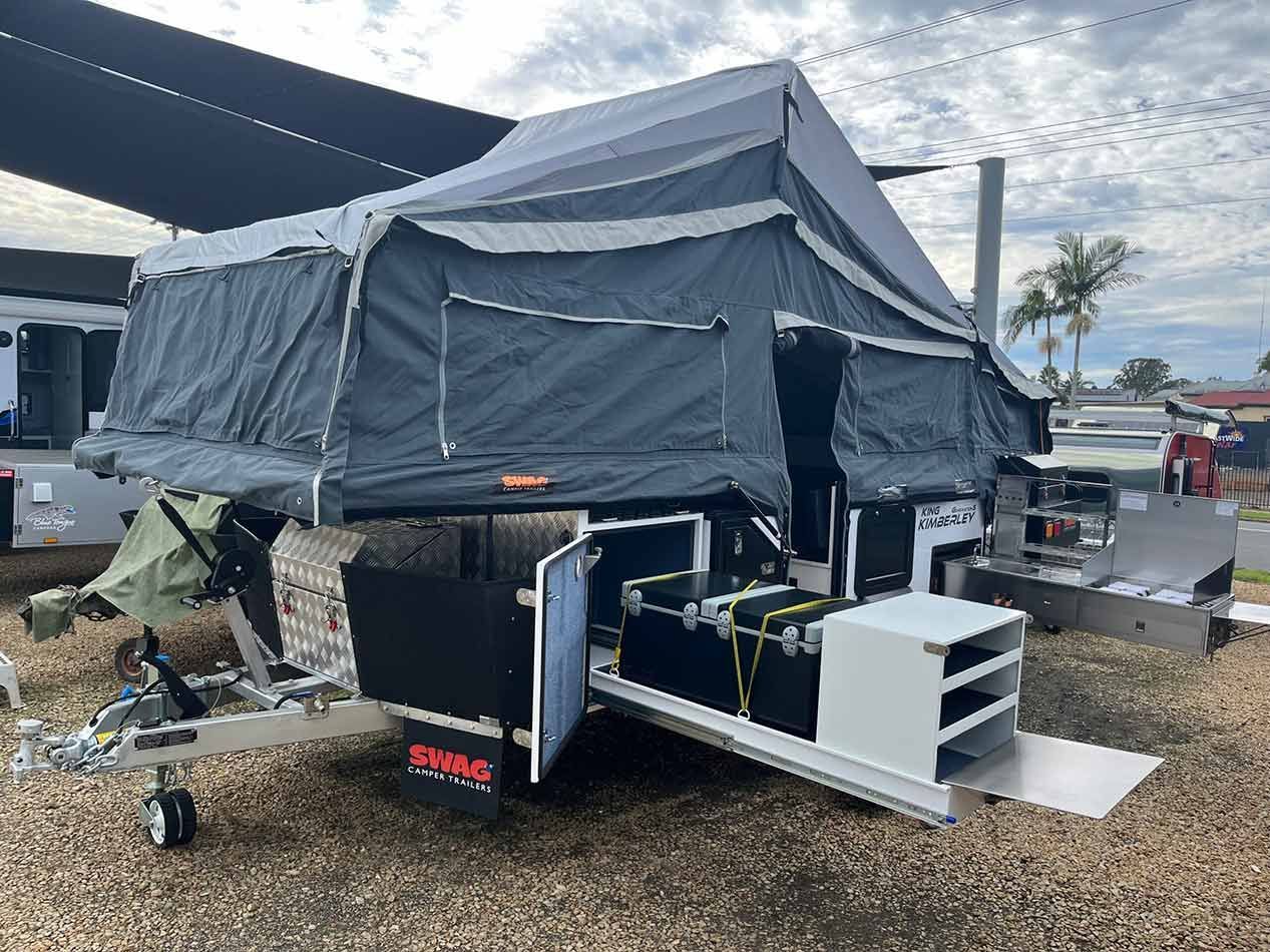 A Camper Trailer With A Tent Attached To It Is Parked In A Gravel Lot — Perkins Caravans in Yamba, NSW